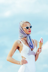 elegant girl in retro swimsuit and trendy sunglasses holding sweet ice cream outdoors