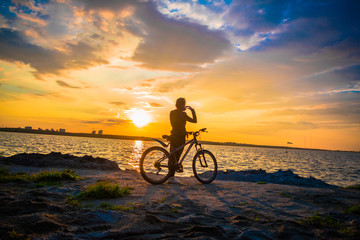 Obraz premium Silhouette of a young woman with a bicycle on the lake at sunset