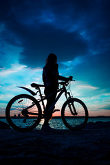 Fototapeta na wymiar Silhouette of a young woman with a bicycle on the lake at sunset