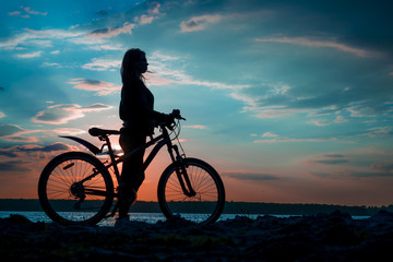 Fototapeta na wymiar Silhouette of a young woman with a bicycle on the lake at sunset
