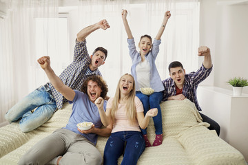A group of friends of fans watching a sports TV sitting on a sofa in the room.