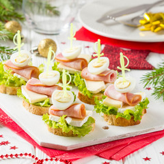 Christmas canapes on bread with brie or Camembert cheese, ham and boiled quail egg. Beautiful presentation on the festive new year's table. Delicious starter