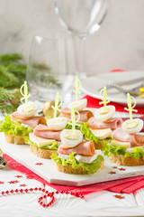 Christmas canapes on bread with brie or Camembert cheese, ham and boiled quail egg. Beautiful presentation on the festive new year's table. Delicious starter