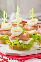 Christmas canapes on bread with brie or Camembert cheese, ham and boiled quail egg. Beautiful presentation on the festive new year's table. Delicious starter