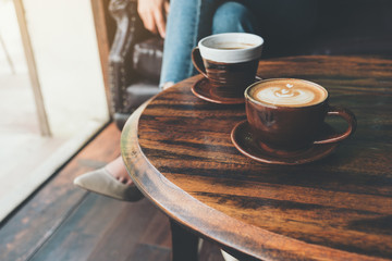 Closeup image of two cups of hot latte coffee on vintage wooden table with woman sitting in background