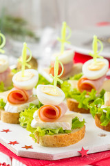 Christmas canapes on bread with brie or Camembert cheese, ham and boiled quail egg. Beautiful presentation on the festive new year's table. Delicious starter