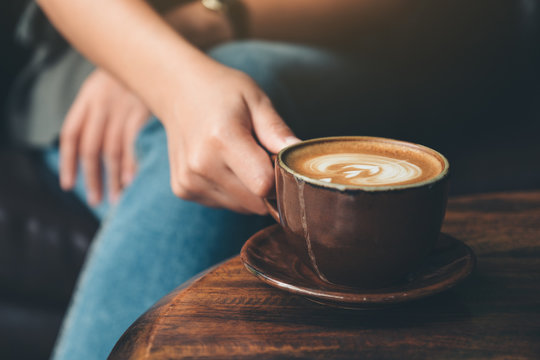 Closeup image of a woman holding  a cup coffee on vintage wooden table in cafe