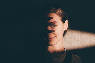 Young woman looking at camera from darkness with light ray on her face