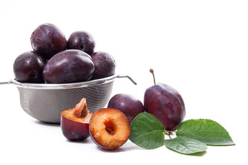 Steel colander with ripe plums, whole and half ripe plums with leaf isolated on a white background..