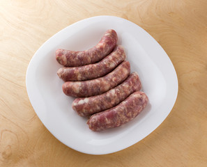 Raw sausages for a barbecue on a white plate. Several barbecue sausages lie next to each other.