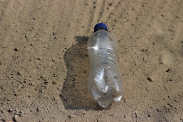  Dropping plastic bottle on sand - symbolising pollution and litter