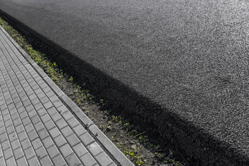 Obraz premium Close-up on a layer of new asphalt at the road under construction with a sidewalk road.