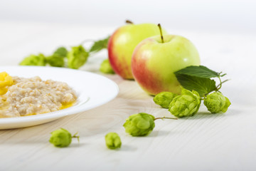 morning  oatmeal porridge abundantly poured creamy melted butter on a white plate among apples and hops. close-up
