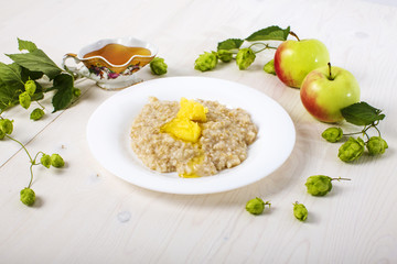 morning breakfast oatmeal porridge abundantly poured creamy melted butter on  white plate among apples and hops and  fresh honey