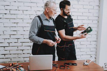 Workers Checking Device in Hands in Repair Shop.