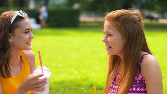 leisure and friendship concept - happy smiling teenage girls or friends drink milk shakes or smoothie at picnic in summer park