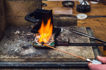 Goldsmith melting down metal with torch equipment to manufacture jewelry