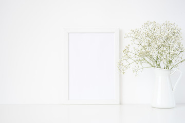 White frame mockup A4 in interior. Frame mock up background for poster or photo frame for bloggers, lettering, art and design. Indoor, frame on table with delicate flowers in jug.. Summer sea mood