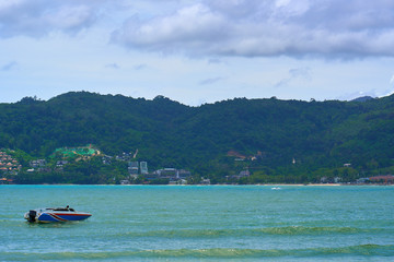 Motor boat sails in turquoise ocean water with green hills landscape of Phuket island in background.  Vacation destination.