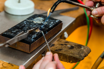 Soldering with a torch flame a jewelry piece at workshop of goldsmith