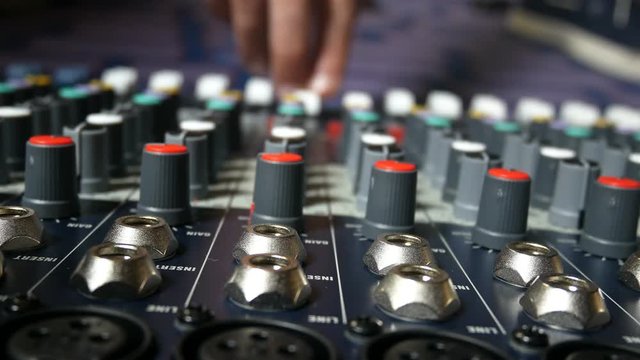 Man adjusting buttons and knobs on audio mixer in music studio indoors close up