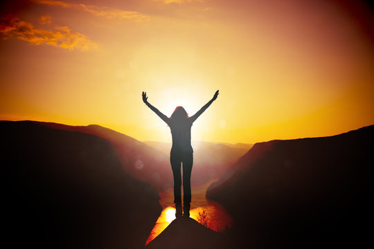 Frau mit ausgebreiteten Armen bei Sonnenuntergang