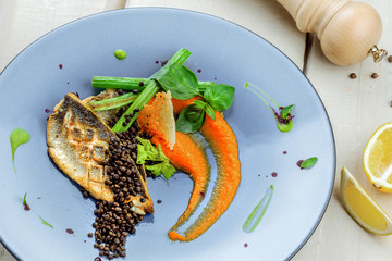 Grilled seabass fish fillet steak with vegetables on a plate. Healthy gourmet seafood meal on a table. Top view close-up shot.