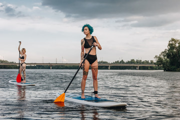 athletic women standup paddleboarding together on river