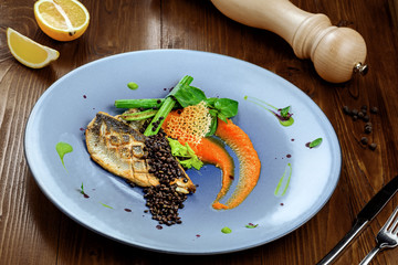 Grilled seabass fish fillet steak with vegetables on a plate. Healthy gourmet seafood meal on a brown wooden table.