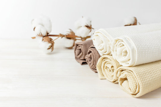 Multicolored clean towels with a branch of cotton on a light wooden background with copy space. Texture of cotton, waffle towel, textiles. Towels for kitchen or Spa concept.