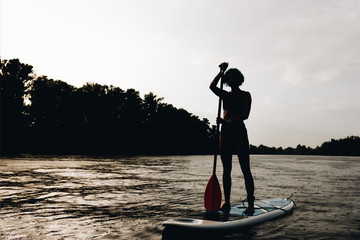 silhouette of sportswoman standing on paddleboard on river