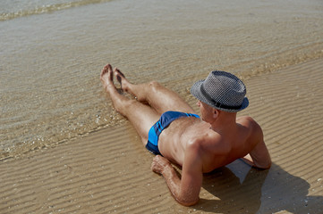 Summer lifestyle portrait of pretty young suntanned man in a hat. Enjoying life and sitting on the...