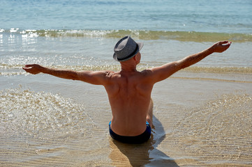 Summer lifestyle portrait of pretty young suntanned man in a hat. Enjoying life and sitting on the...