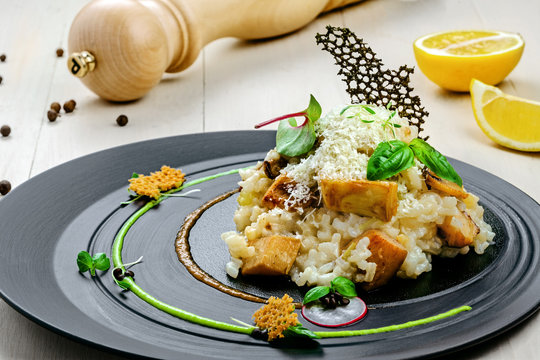 Tasty risotto cooked in a vegetable broth with porcini mushrooms and parmesan cheese on a beautiful plate. First class Italian dish on a wooden table. Close-up shot.