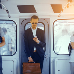 Businessman standing in subway and holding his bag. Young handsome man wearing full suit and round...