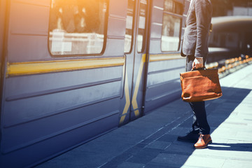 Businessman standing on platform at train station. Cropped picture of man in stylish suit holding leather bag in his hand while standing in front of blue subway train.