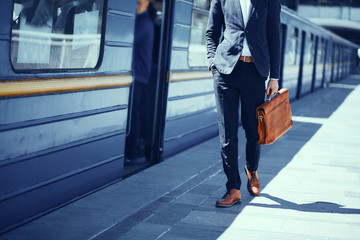 Businessman standing at subway platform. Elegant guy in formal suit and brown leather shoes...