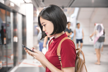 Beautiful young woman traveler using smartphone at a train station , Transportation and travel lifestyle concept