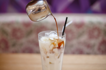 Barista prepares summer cold coffee with ice and milk in transparent glass.