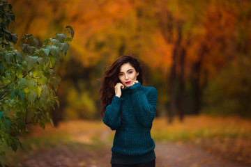 Happy young woman in park on sunny autumn day. Cheerful beautiful girl in green sweater outdoors among yellow leaves on beautiful fall day.