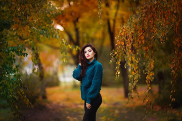 Happy young woman in park on sunny autumn day. Cheerful beautiful girl in green sweater outdoors among yellow leaves on beautiful fall day.