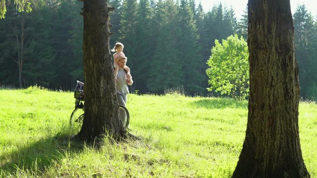 A young man carries a little girl around his neck and rolls a bicycle with a child seat on a forest path. Father watches the gps map signal on the smartphone.