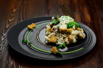 Tasty risotto cooked in a vegetable broth with porcini mushrooms and parmesan cheese on a beautiful plate. First class Italian dish on a wooden table.