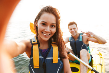 Loving couple kayaking on lake sea in boat make selfie by camera. - obrazy, fototapety, plakaty