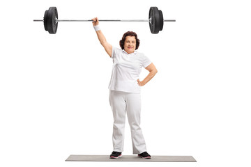 Mature woman on standing on an exercise mat and lifting a barbell with one hand