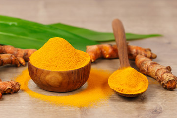 Turmeric powder in wooden bowl  and fresh turmeric on old wooden table. Indian Spices