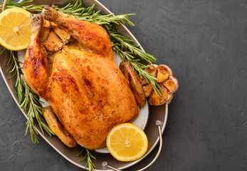 Roasted chicken with rosemary served on a metal plate with lemon on black table. Christmas turkey. Copy space. Top view.