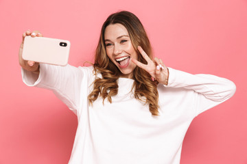 Photo of cheerful brunette woman with beautiful long hair showing peace sign and taking selfie on...