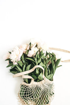 White Peony Flowers In String Bag On White Background. Flat Lay, Top View Minimal Festive Floral Concept.