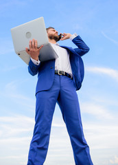 Man well groomed businessman holds laptop while speak phone blue sky background. Guy formal suit modern technology manager entrepreneur answer phone call. Communicating skill. Always in touch